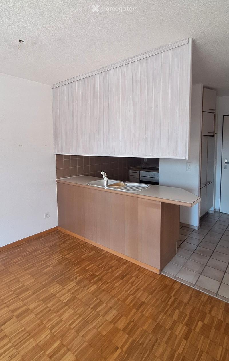 Empty kitchen with wooden flooring, light-colored cabinets, and a sink area. No appliances or furniture are present.