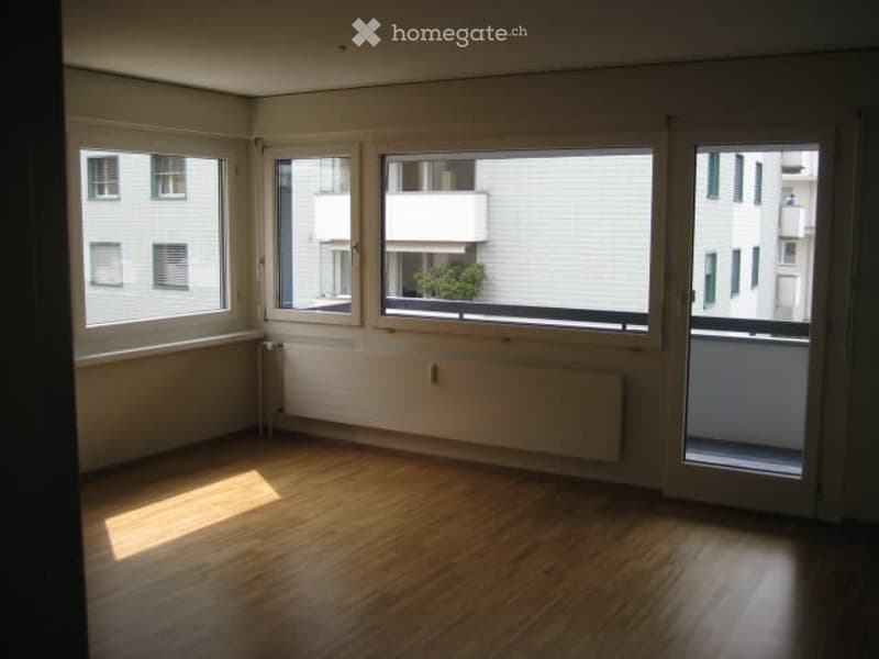 Empty room with wooden flooring, large windows, and a balcony door leading to a small balcony area.