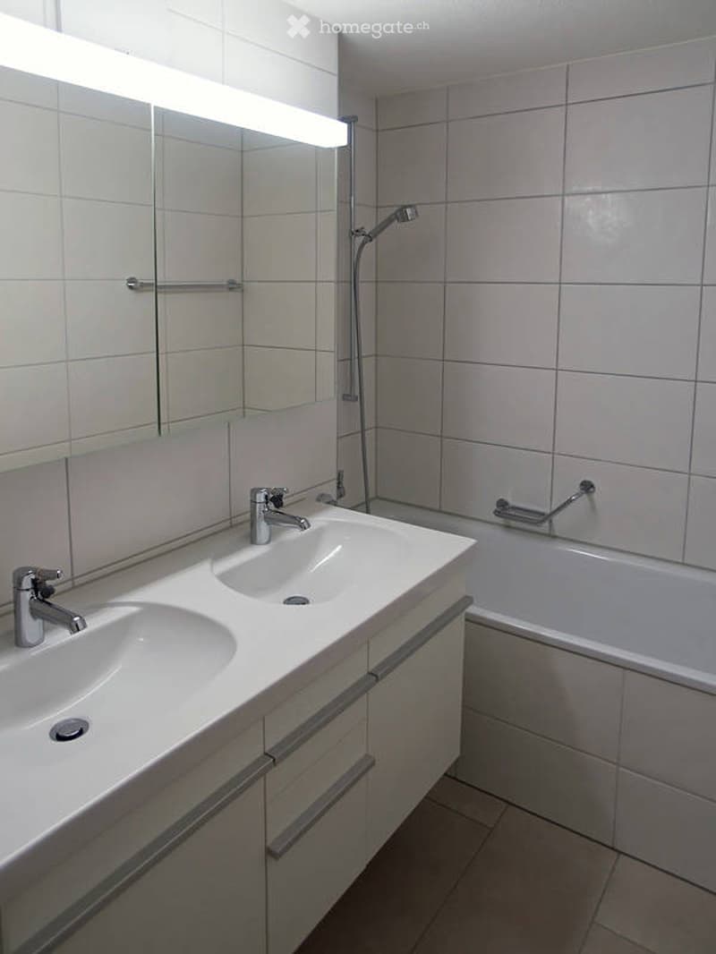 Modern bathroom with white tiles, double sink, mirror, bathtub, and showerhead.