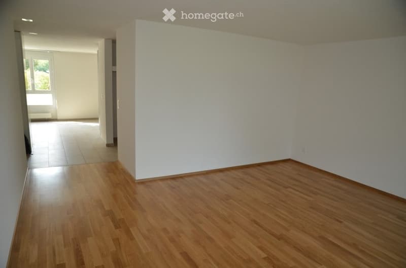 Empty room with wooden flooring and white walls, featuring a large window and a doorway leading to another space.