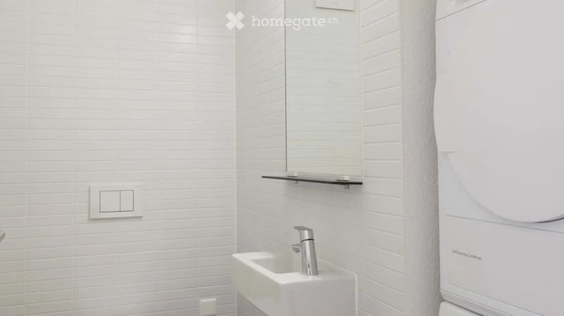Modern bathroom with white tiled walls, a white sink with a chrome faucet, a mirror above the sink, and a shelf for storage.