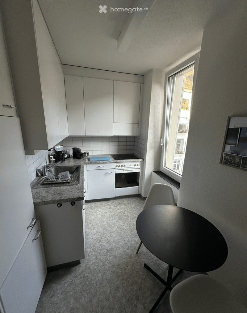 Modern kitchen with white cabinets, a sink, stove, and a small dining area with a round table and chairs.