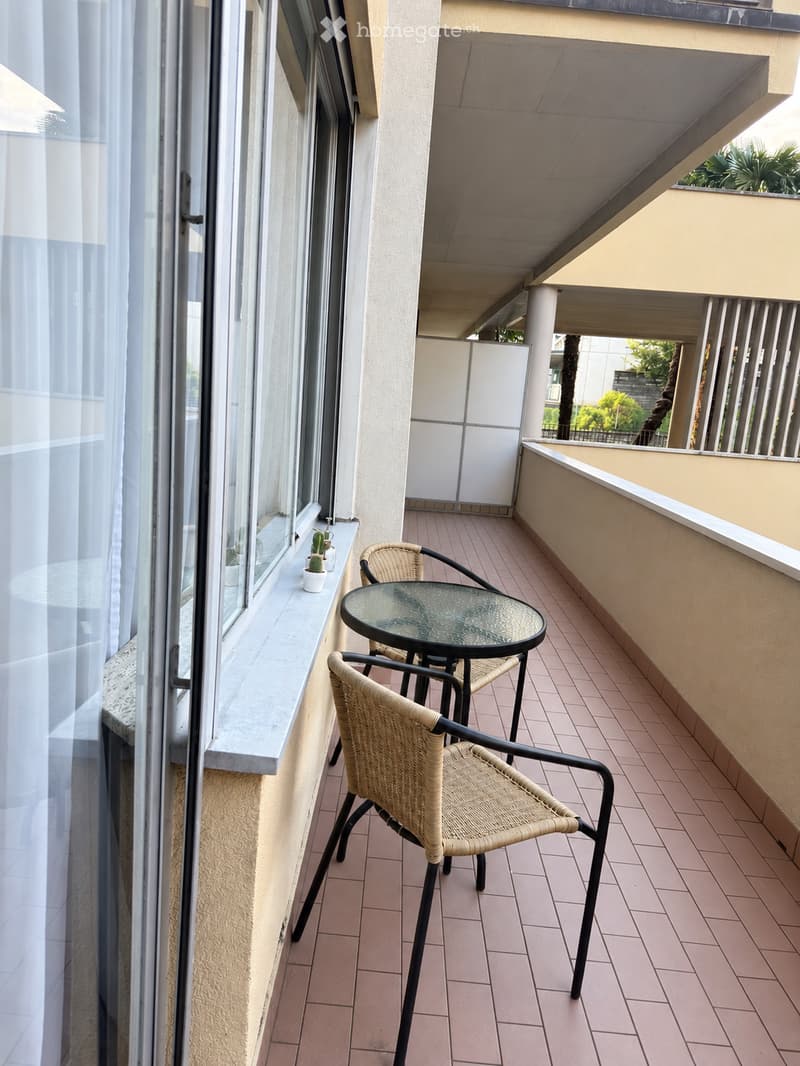 Balcony with tiled floor, glass table, wicker chairs, and small potted plants on the windowsill.