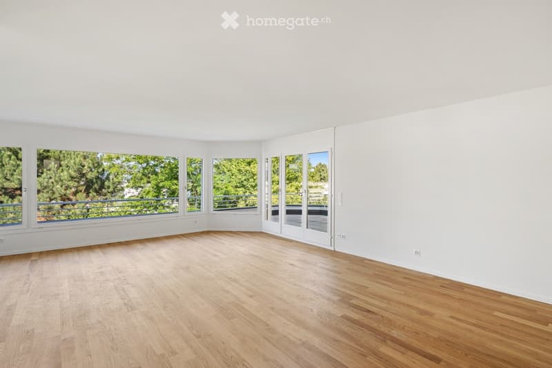 Bright, empty room with wooden flooring, large windows, and sliding glass doors leading to a balcony.