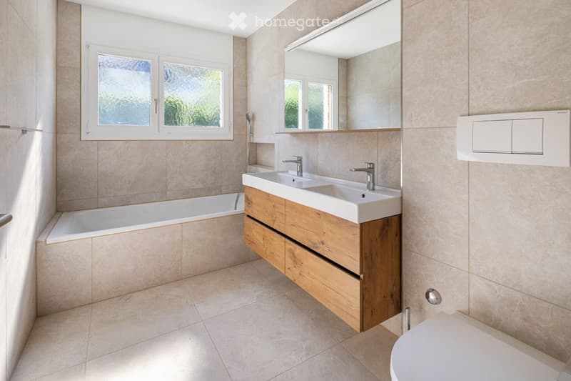 Modern bathroom with a double sink vanity, bathtub, large mirror, and tiled walls.