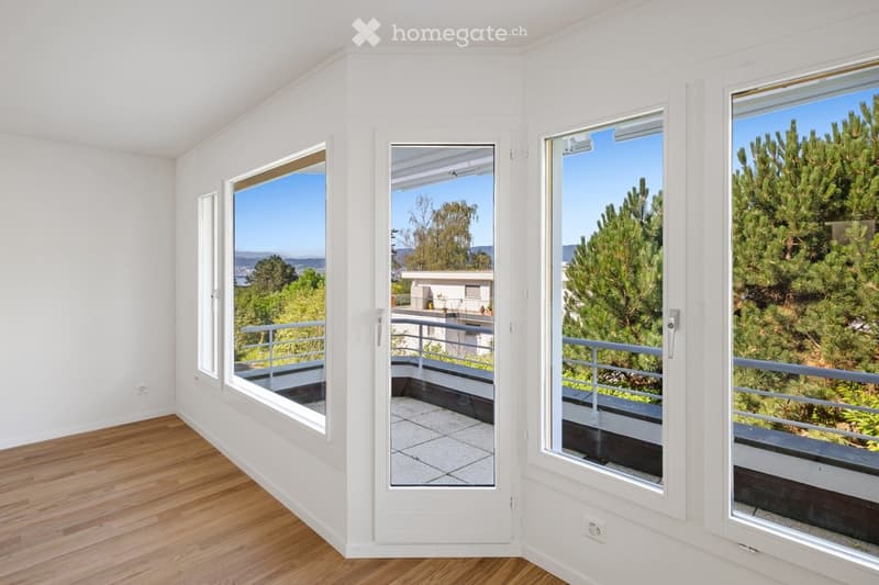 Empty room with wooden flooring, large windows, and a view of trees and a distant landscape.