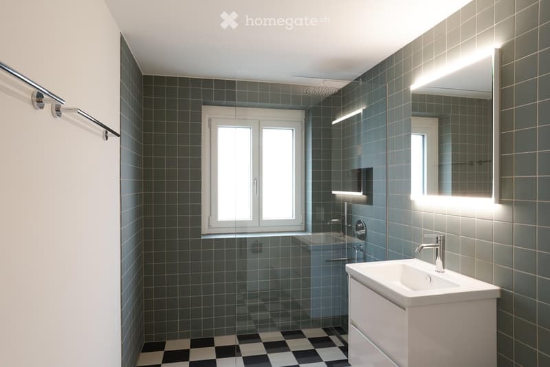 Bathroom with checkered floor, glass shower enclosure, a white sink with a faucet, tiles, and mirrors.