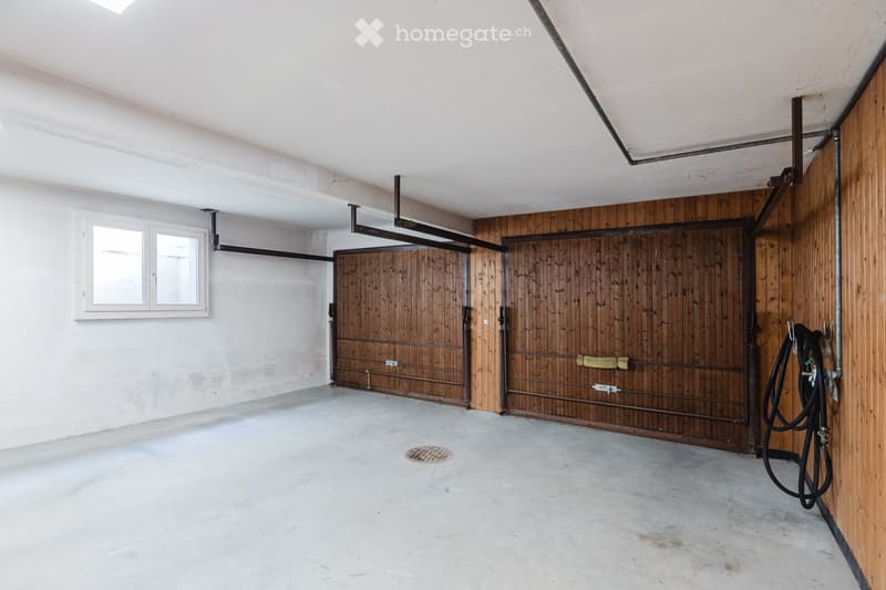 Empty garage with concrete floor, white walls, wooden doors, and a small window. No furniture or equipment present.