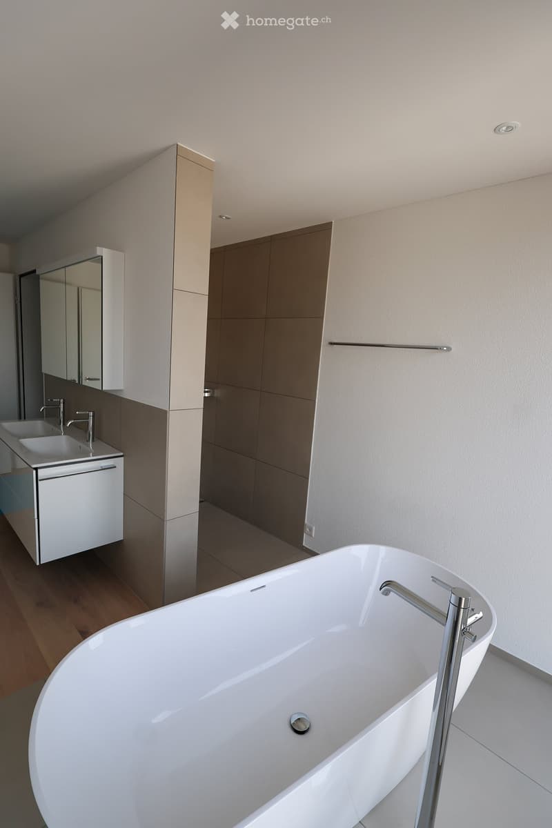 Modern bathroom with a large freestanding bathtub, double sink vanity with mirrors, and sleek cabinetry.