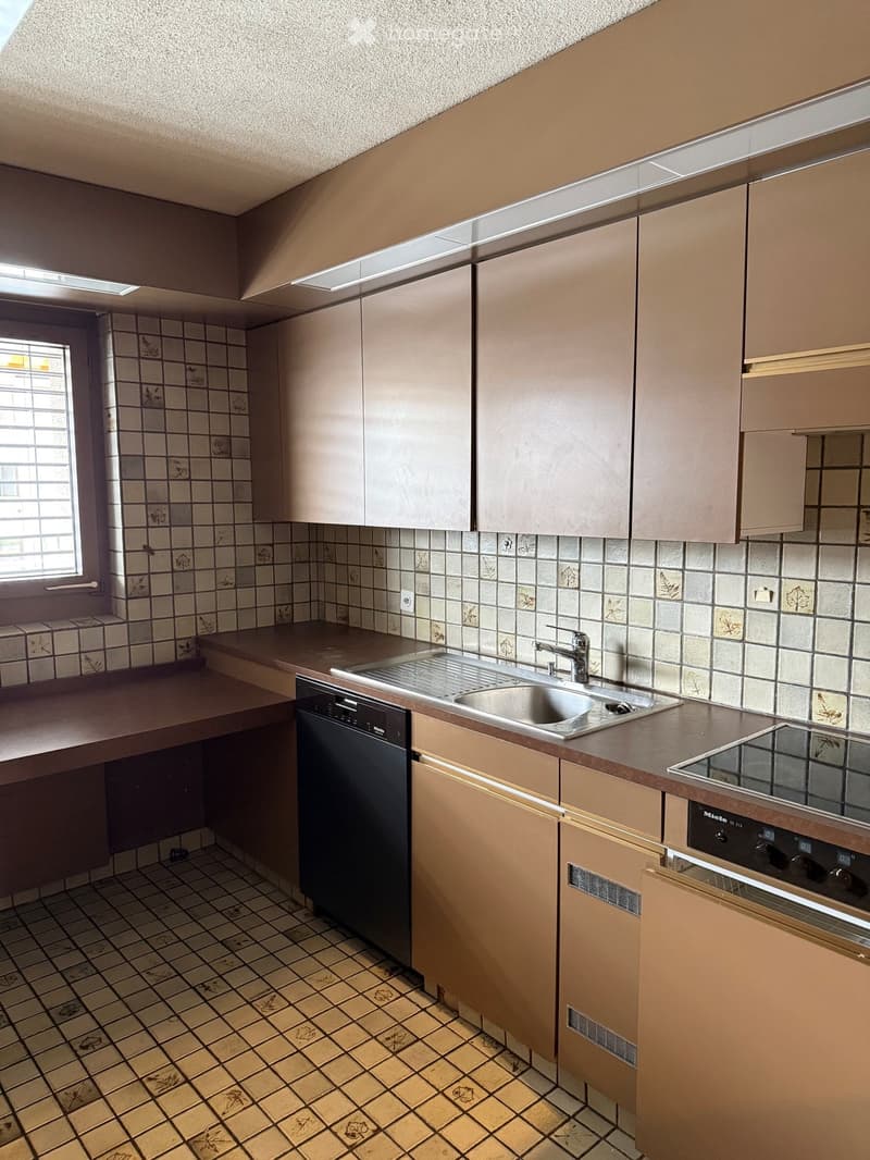 Kitchen with beige cabinets, tiled walls and floor, stainless steel sink, dishwasher, and electric stove.