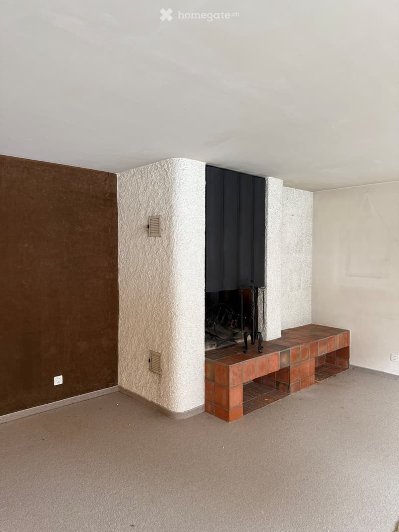 Empty room with a fireplace, a bench, and a tiled floor. The walls are painted in neutral tones, and the ceiling is white.