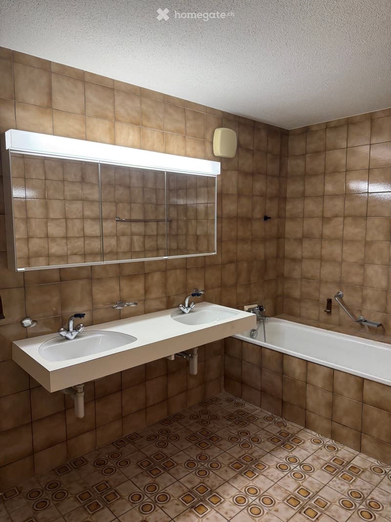 Bathroom with two sinks, a bathtub, a large mirror, and tiled walls and floor.