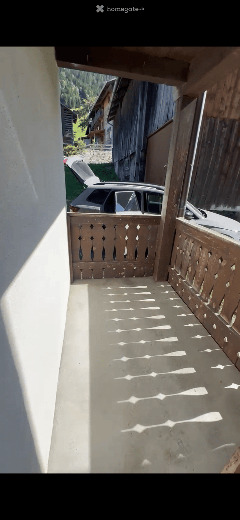 Balcony with wooden railing, overlooking a rural area with houses and greenery.