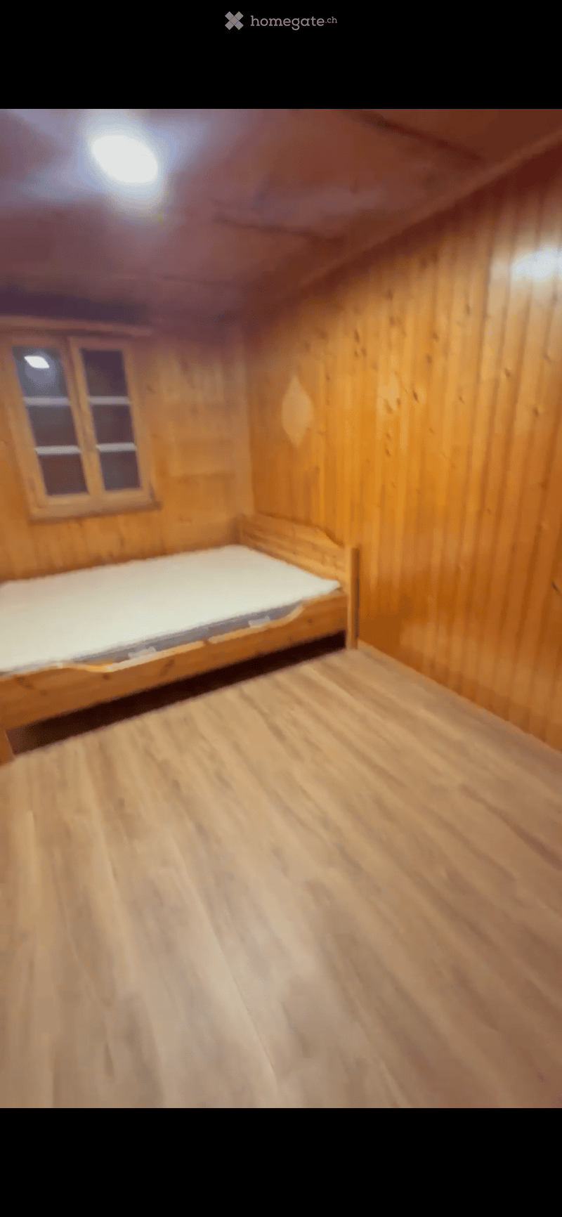 Cozy wooden bedroom with a single bed, wooden walls, and a small window.