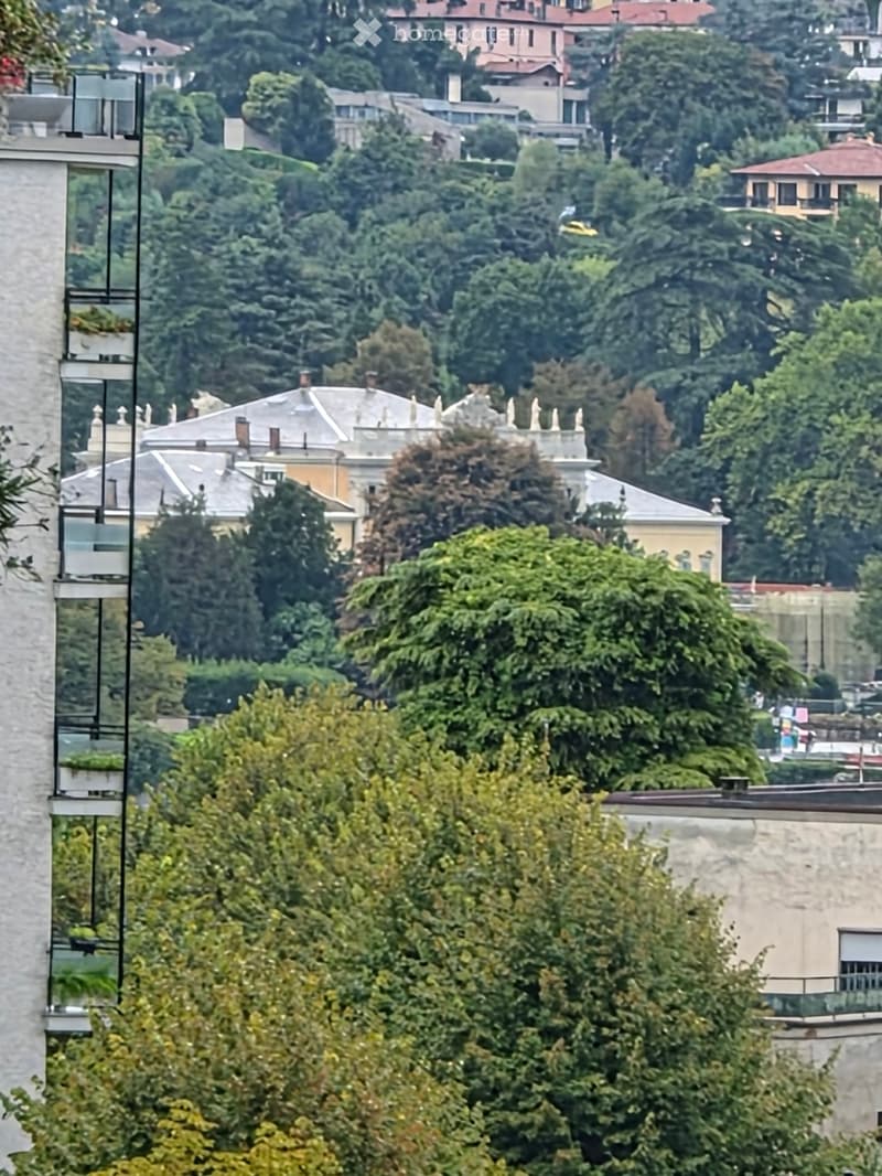 View from a balcony showing a lush green landscape with trees and distant buildings in the background.