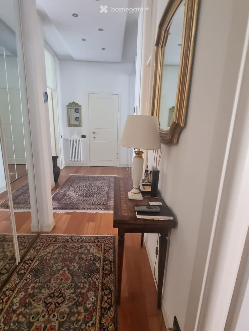 Elegant hallway with wooden flooring, a small table with a lamp, and a large ornate mirror on the wall.