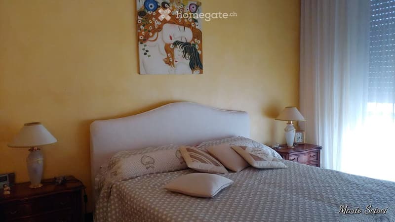Cozy bedroom with a large bed, decorative pillows, two nightstands with lamps, and a colorful painting on the wall.