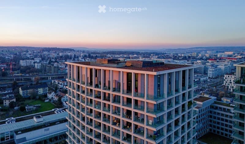 Modern high-rise building with balconies and large windows, overlooking a cityscape at sunset.