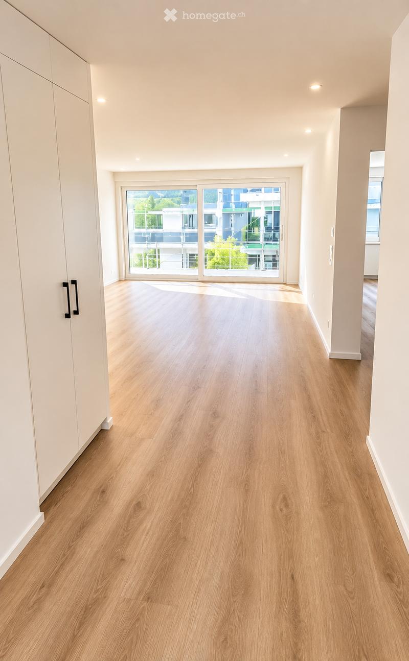 Empty hallway with light wooden flooring, white walls, and a large glass door leading to a balcony or outdoor area.
