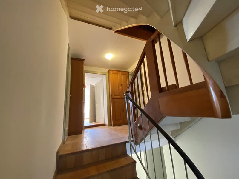 Spiral staircase with wooden steps and metal railing, leading to a hallway with tiled floor and wooden cabinet.