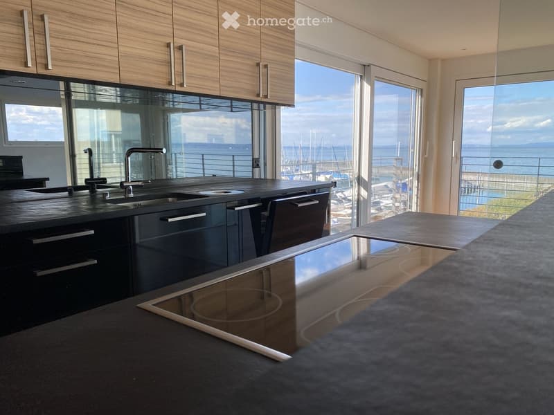 Modern kitchen with dark countertops, stainless steel sink, induction cooktop, and large windows offering a view of the harbor.