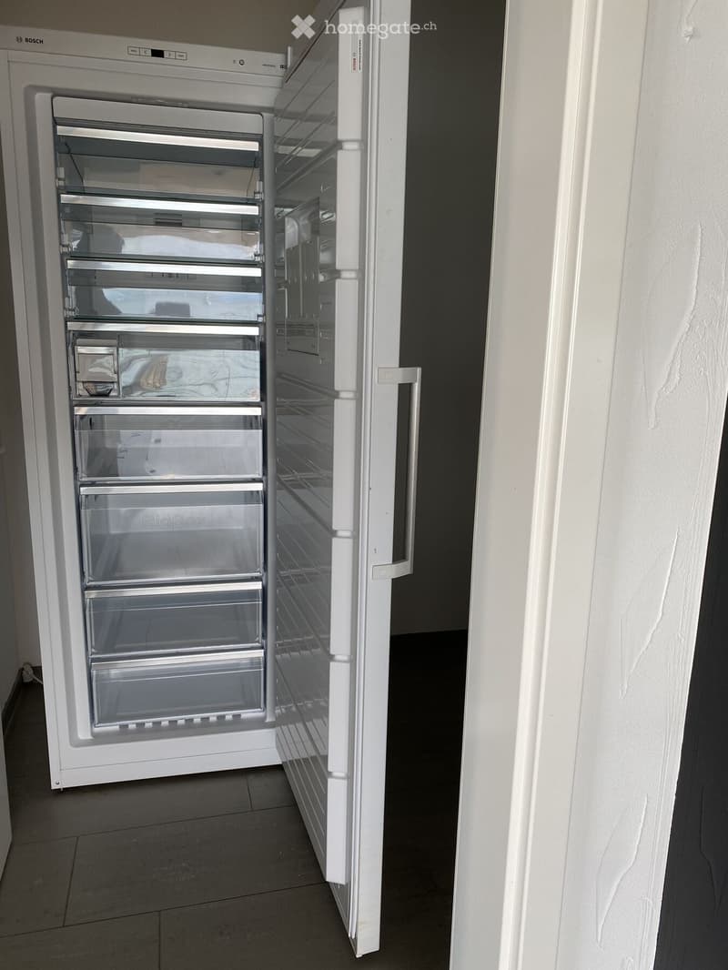 Modern white refrigerator with multiple glass shelves and compartments, fully empty, placed against a white wall.