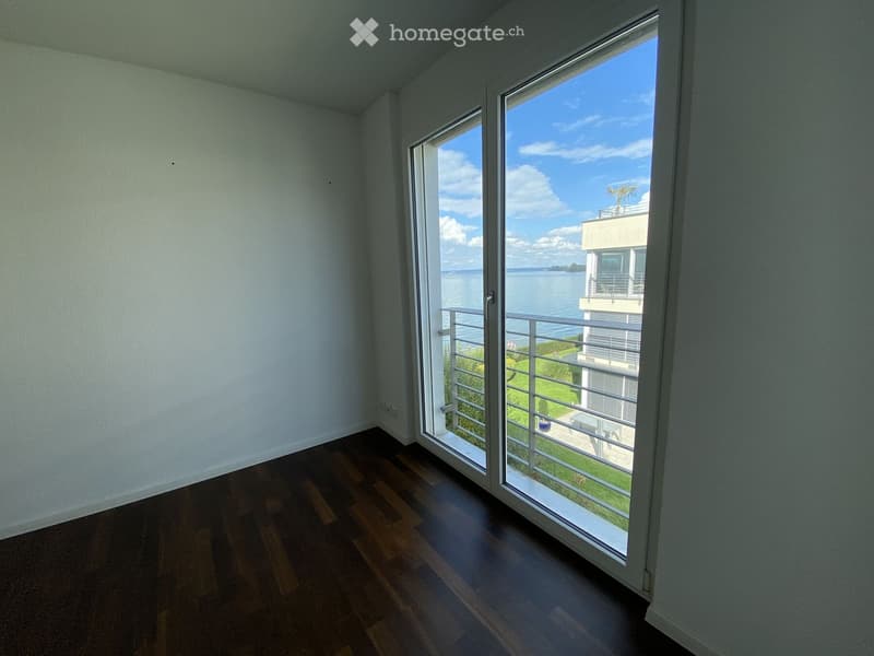 Empty room with wooden flooring and large sliding glass doors leading to a balcony overlooking a body of water.