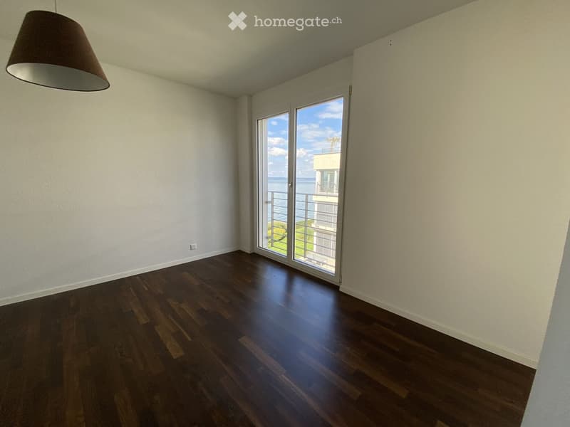 Empty room with dark wooden flooring, white walls, and large sliding glass doors leading to a balcony with a scenic ocean view.