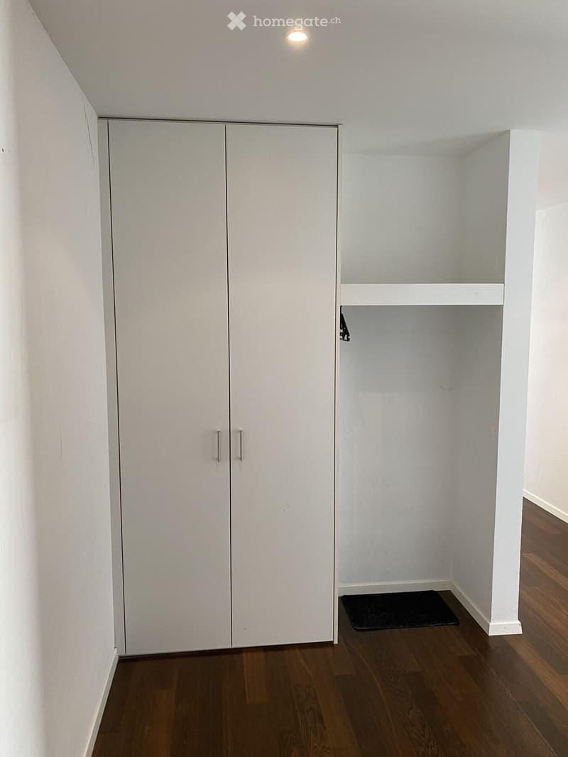 Empty room with wooden flooring, white walls, built-in closet with double doors, and a small open shelving unit.