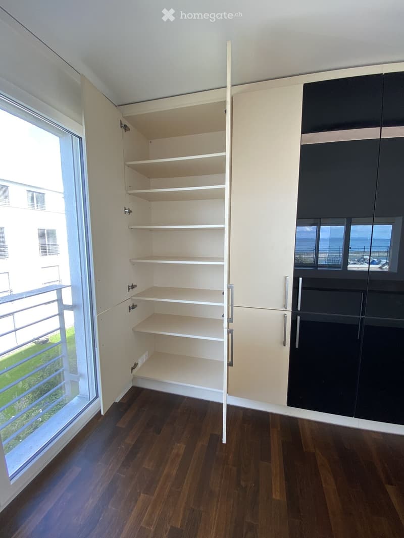 Empty room with wooden flooring, white walls, and built-in storage units with open shelves and closed cabinets.