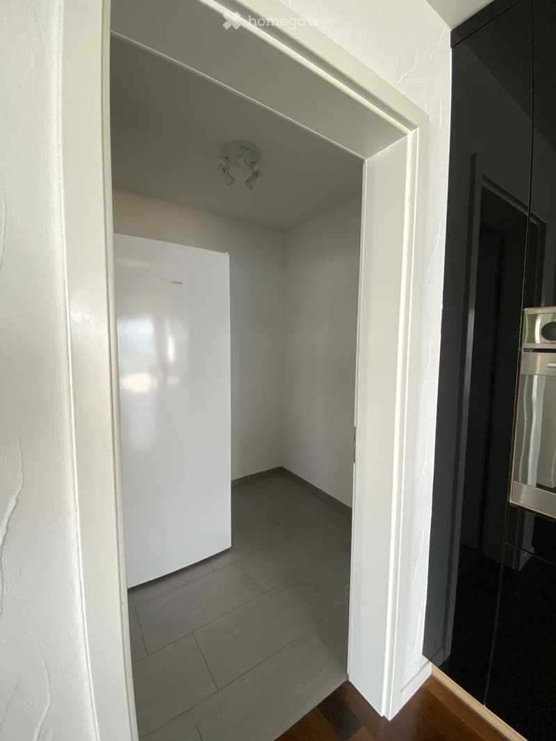 Empty room with tiled floor, white walls, and a white refrigerator visible in the background. No furniture or personal items present.