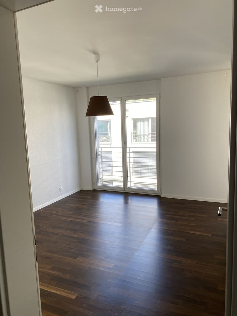Empty room with wooden flooring, white walls, and a large sliding glass door leading to a balcony.