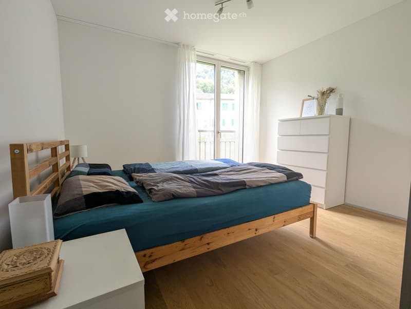 Modern bedroom with a wooden bed, blue bedding, a white nightstand, and a white dresser with a vase and picture frame on top.