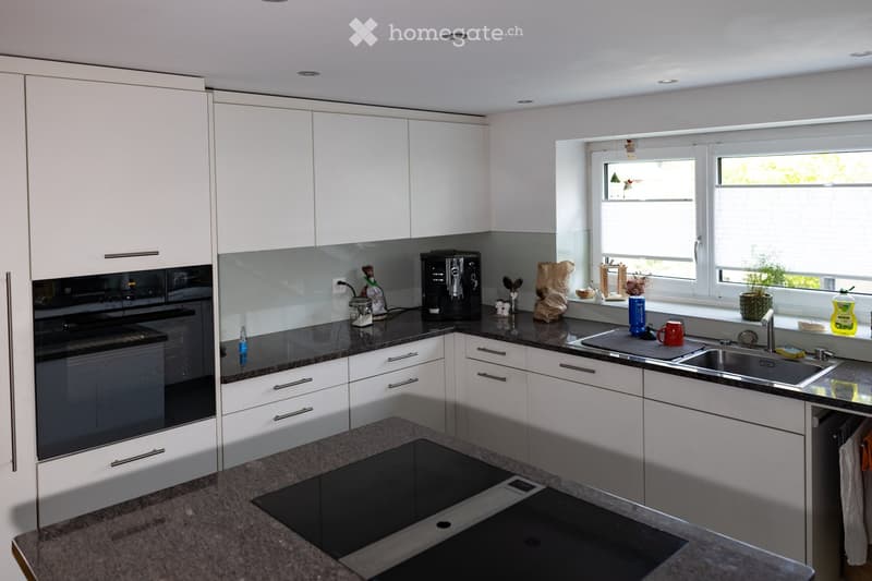 Modern kitchen with white cabinets, granite countertops, stainless steel sink, and various appliances including an oven and coffee maker.