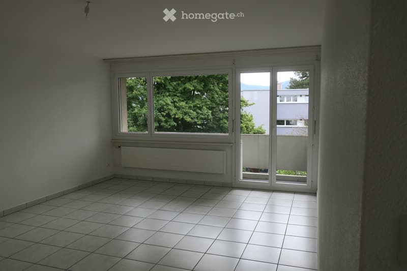 Empty room with tiled floor, large windows, and sliding glass doors leading to a balcony area.