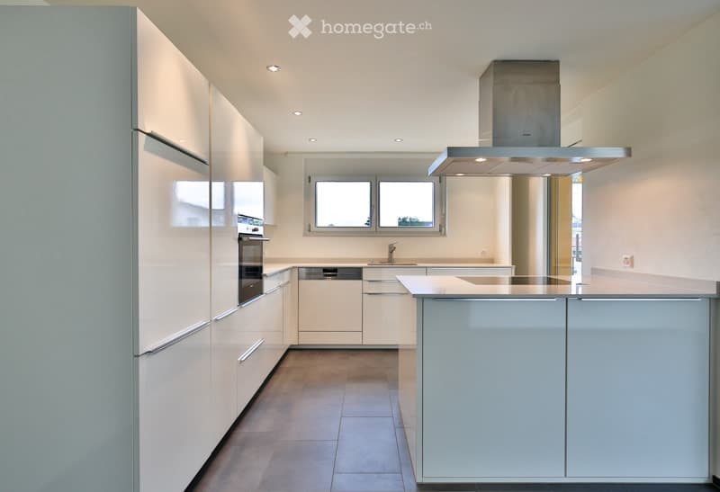 Modern kitchen with white cabinets, stainless steel appliances, island, and large windows.