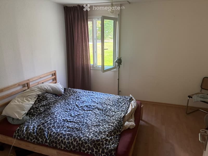 Bedroom with a wooden bed, leopard print bedspread, pillows, a chair, and a window with curtains.