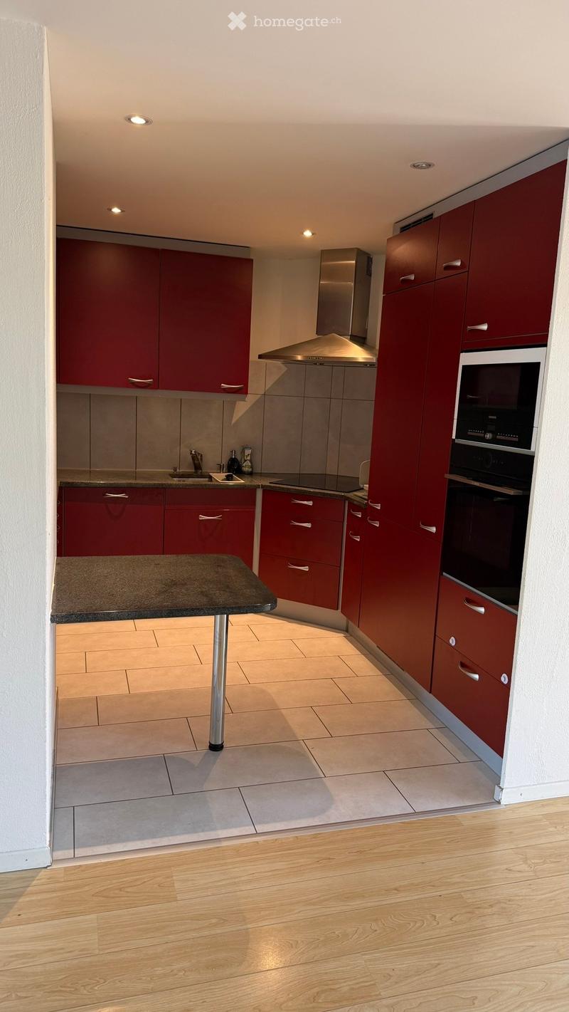 Modern kitchen with red cabinets, stainless steel appliances, and a central island table.