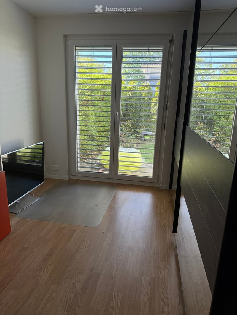 Empty hallway with wooden flooring, large glass doors leading to a balcony, and a view of greenery outside.