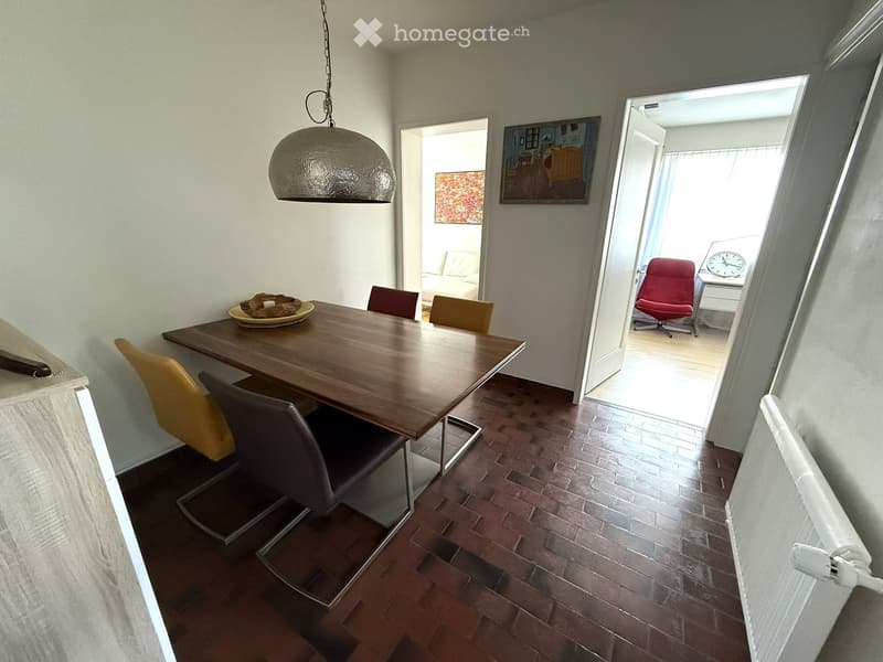 Dining area with a wooden table, chairs, and a clock visible in the adjacent room.