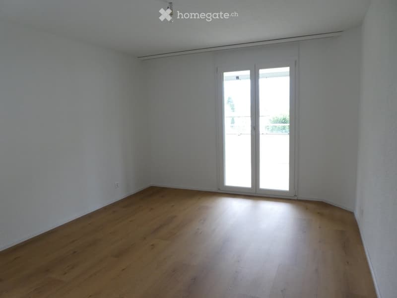 Empty room with wooden flooring, white walls, and large sliding glass doors leading to a balcony.