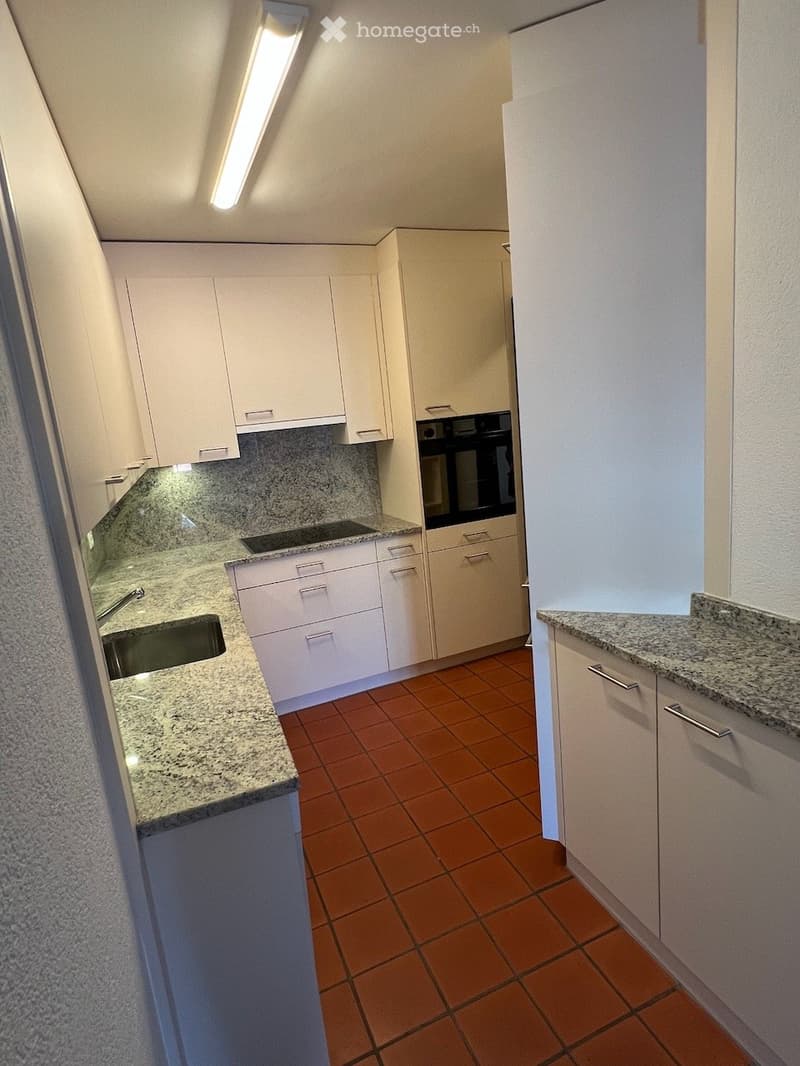 Modern kitchen with white cabinets, granite countertops, and a stainless steel sink. Features include a built-in oven and a tiled floor.