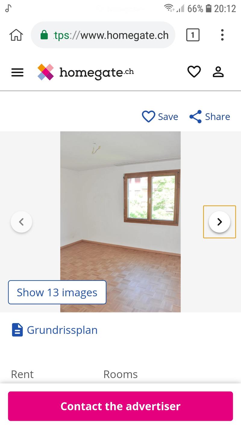 Empty room with wooden flooring and white walls, featuring a large window with wooden frame and a visible light fixture on the ceiling.