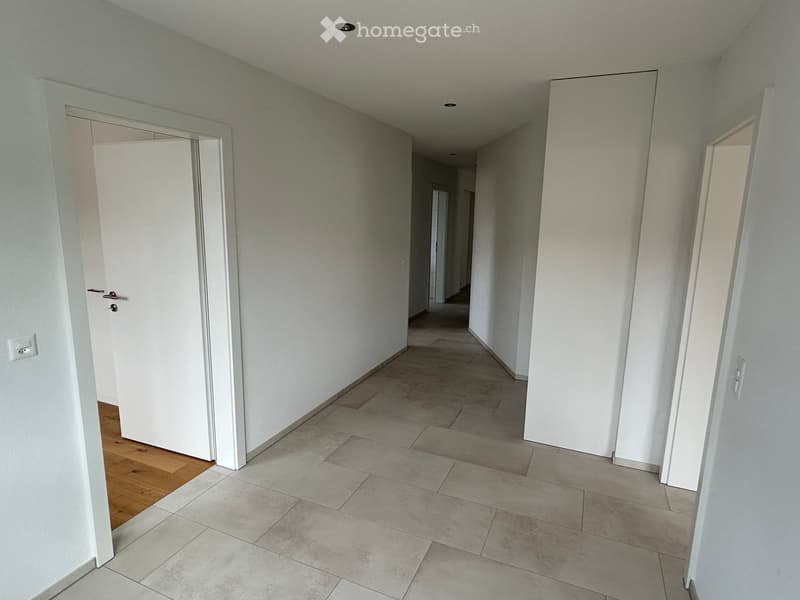Empty hallway with tiled floor and white walls, featuring several doors and recessed lighting.