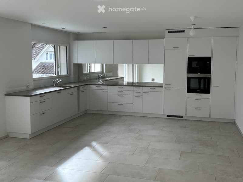 Modern kitchen with white cabinets, stainless steel sink, and built-in oven. Features tiled flooring and large windows.