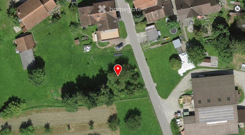 Aerial view of a rural residential area with multiple houses, green lawns, trees, and a road running through the neighborhood.