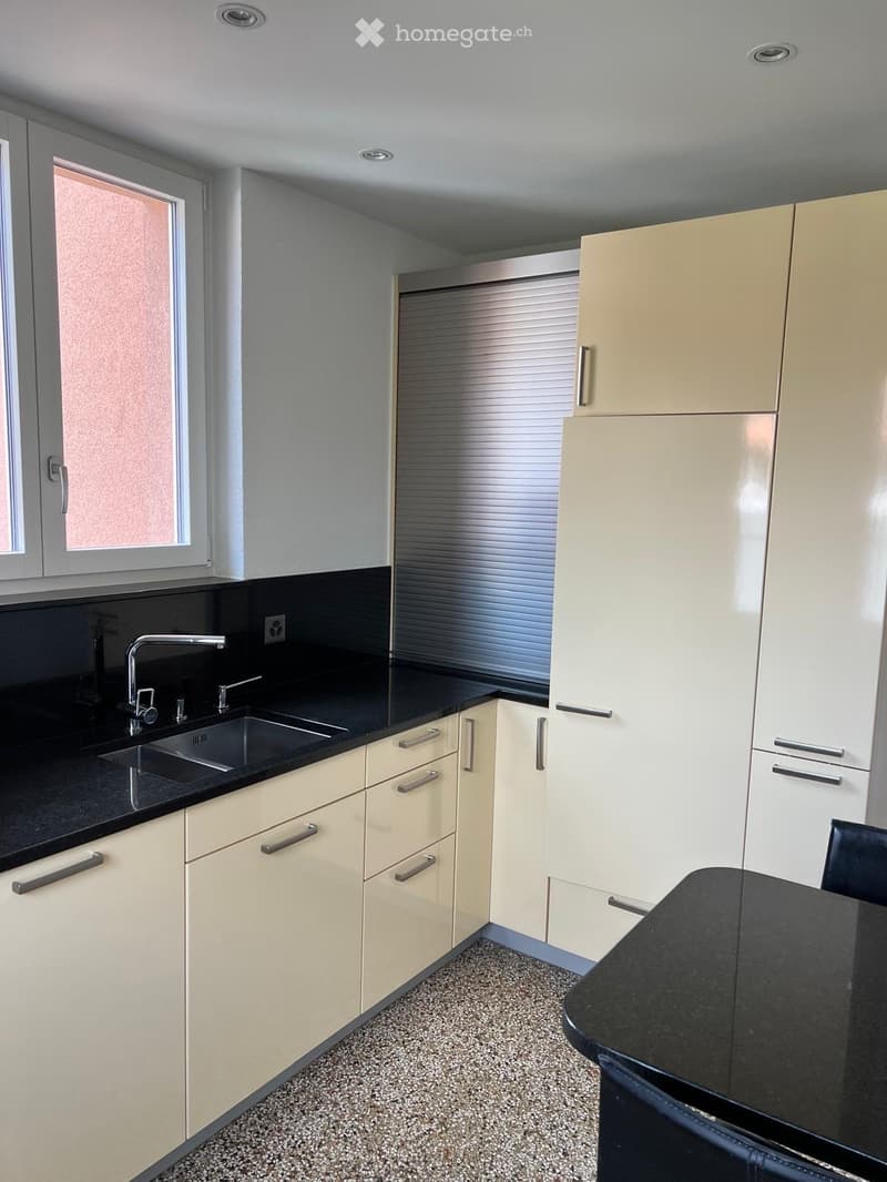 Modern kitchen with light-colored cabinets, black countertops, a sink, and a chair near the counter.