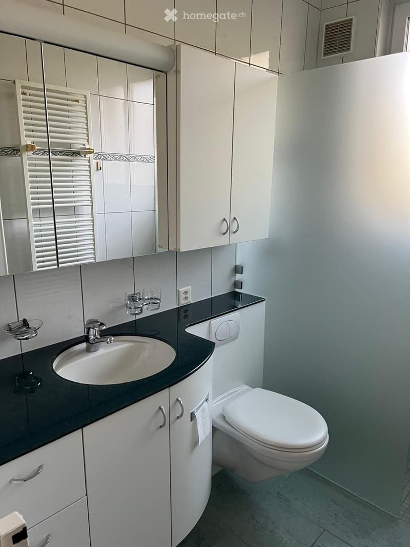 Modern bathroom with white cabinets, black countertop, sink, faucet, toilet, and a mirror above the sink. Two cups are placed on the countertop.