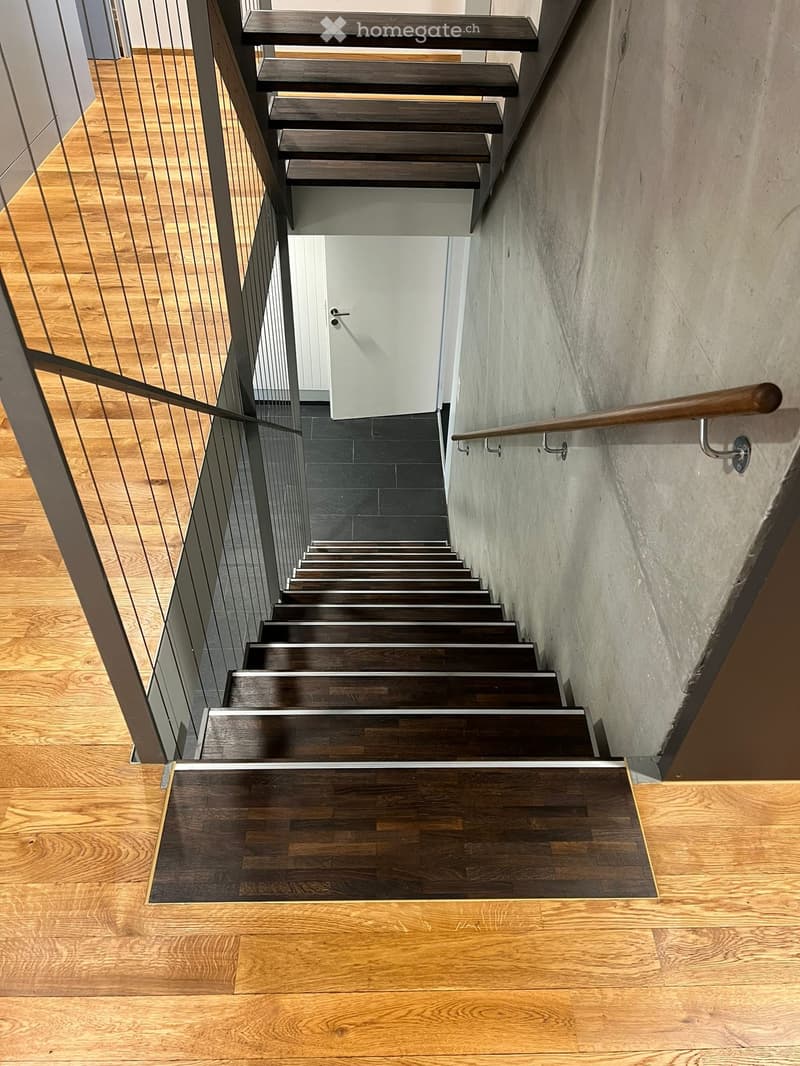 interior staircase with dark wood steps and silver metal railing, concrete wall, wooden floor