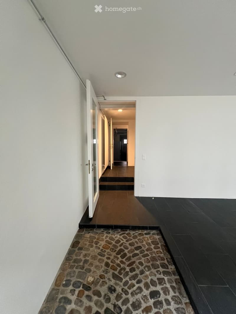 Empty corridor with stone flooring, white walls, and an open door to a room.